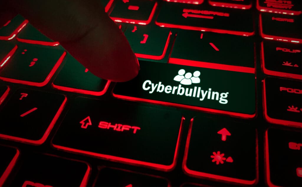 A person pressing a key on a keyboard with an icon of people and the word "cyberbullying."