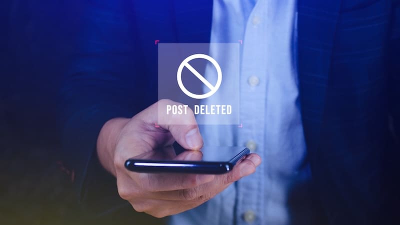 A person holds a smartphone displaying a "post deleted" icon, suggesting content removal or censorship on a digital platform. the image captures a moment of technology interaction.