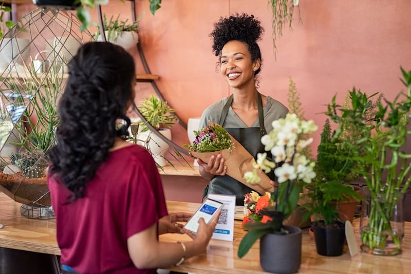 Storeowner giving flowers to a customer while smiling.