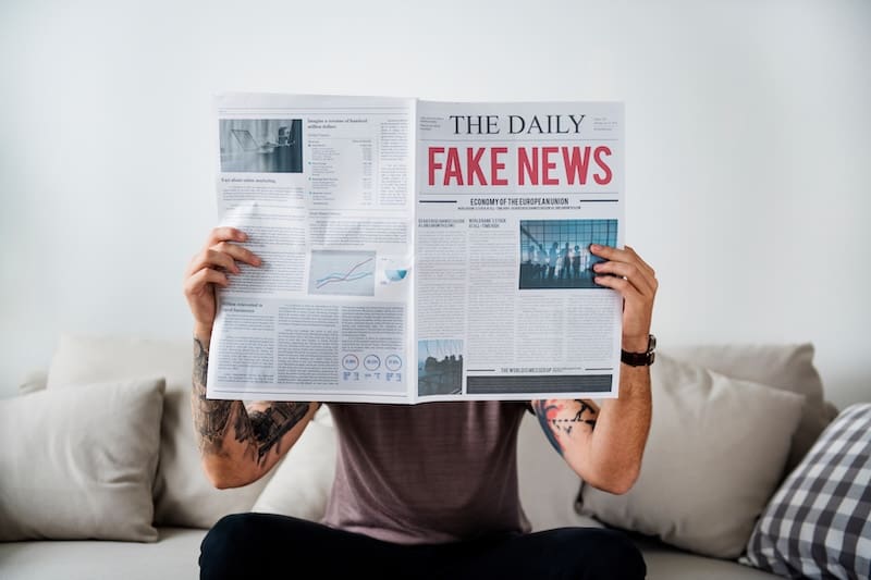 Fake news headline on a newspaper with a person holding it up in front of them.