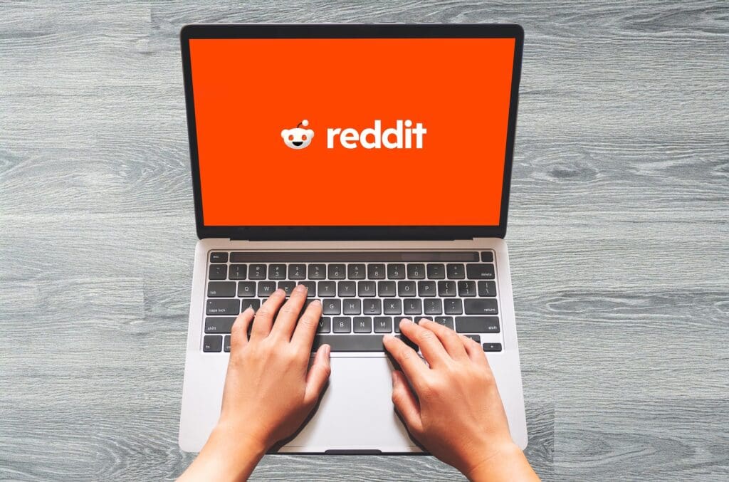 A person's hands on the keyboards of a laptop with Reddit on the screen.