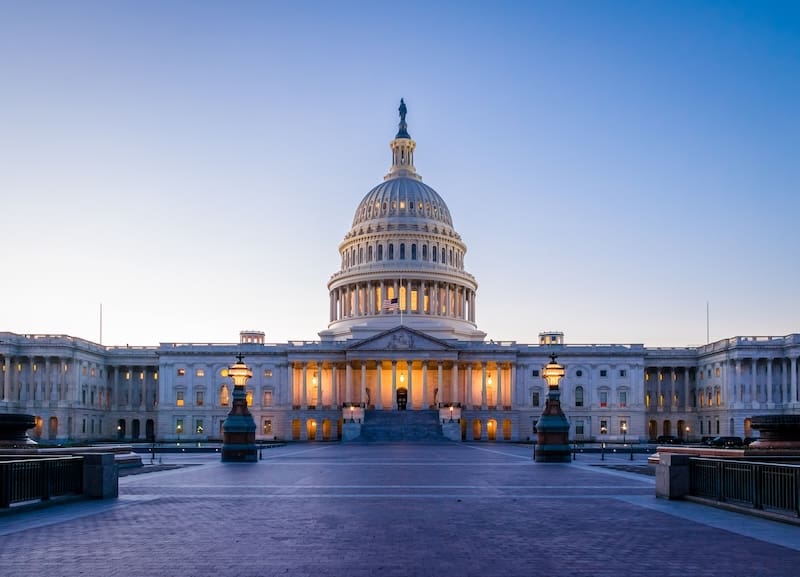 The United States Capitol building at dusk, its dome and exterior lights illuminated against a clear blue sky, stands as a symbol of democracy and the ongoing fight against harmful online content.