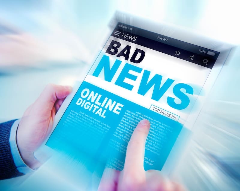 A person holds a tablet displaying a digital newspaper with the large headline "BAD NEWS" and sections labeled "ONLINE" and "DIGITAL." The scene has a blue tint and a blurred motion effect.