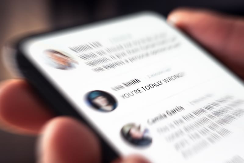 A person holding a smartphone displaying a blurred online conversation, with a clear message saying “YOU’RE TOTALLY WRONG!” indicating an argument or disagreement in a chat.
