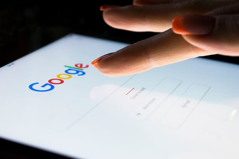 A close-up of a person using a tablet with the Google homepage displayed, focusing on their fingers with orange nail polish interacting with the screen for online reputation management tasks.