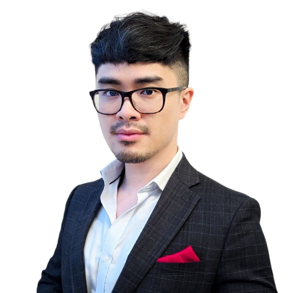 A man with short, dark hair and glasses, wearing a dark checkered suit, white shirt, and a red pocket square, stands against a plain white background—presenting a polished team leader look.
