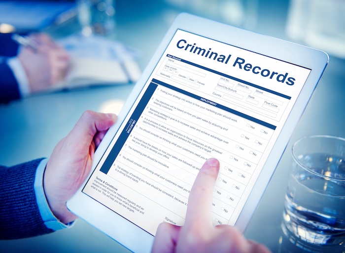 A person holding a tablet with the word "criminal records" on it, allowing users to find mugshots.