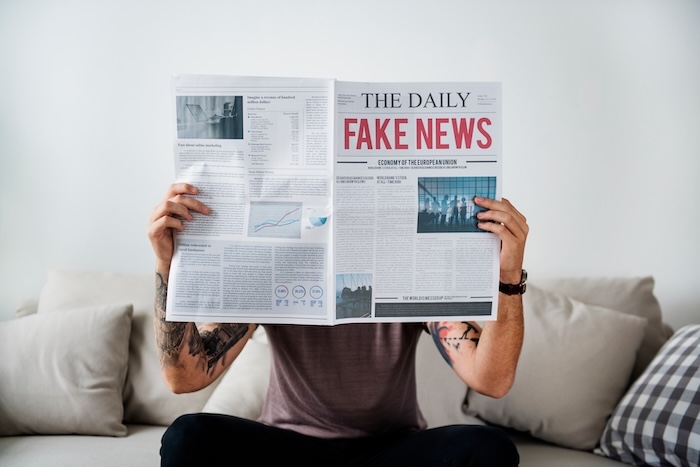 A man holding up a fake news newspaper on a couch, depicting the negative impacts of social media on business.