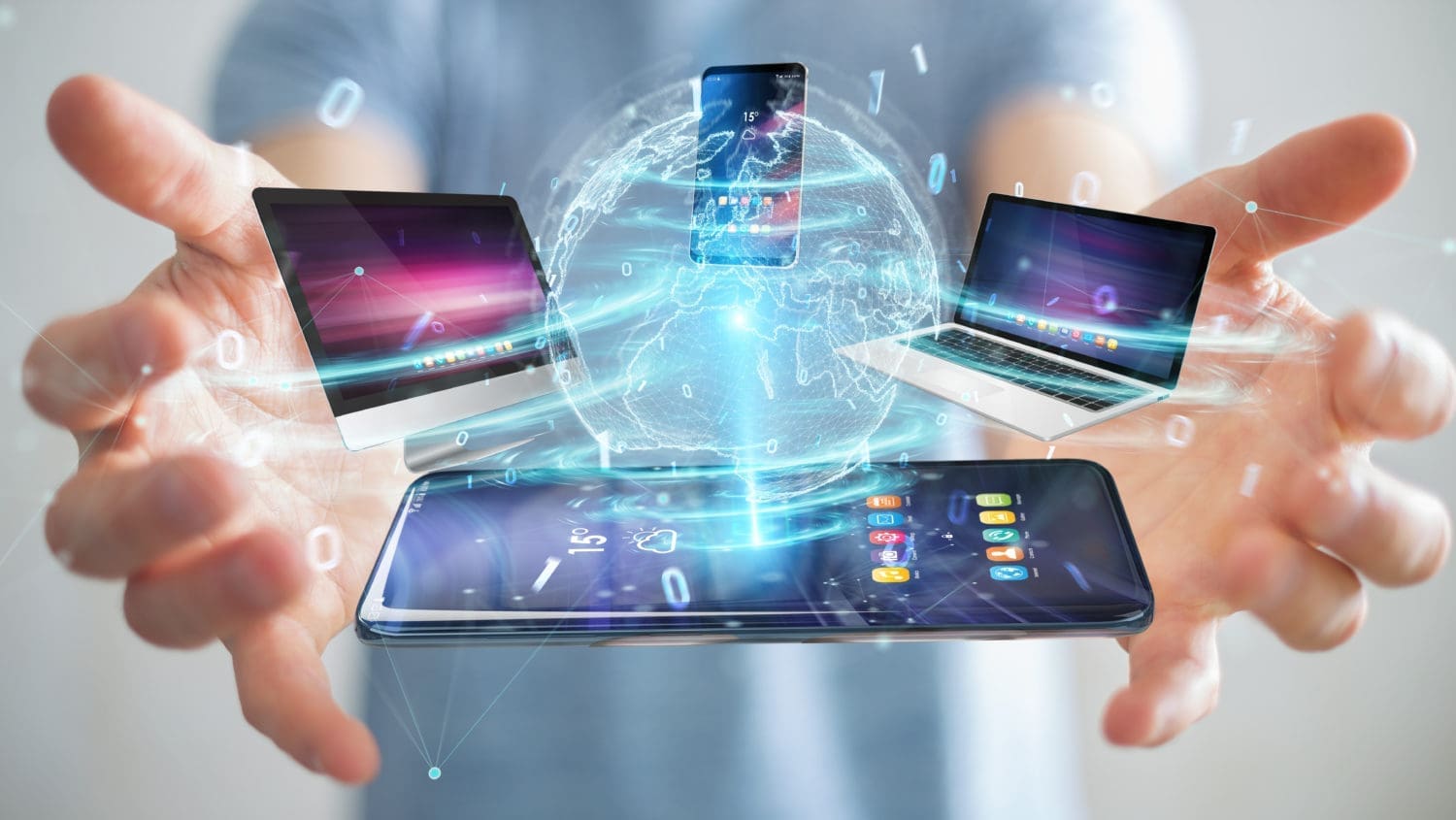 A man's hands holding a laptop, tablet, and smartphone.