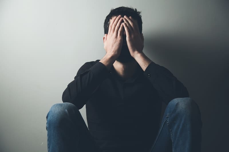 A man covering his face with his hands, desperately seeking to restore his online reputation.