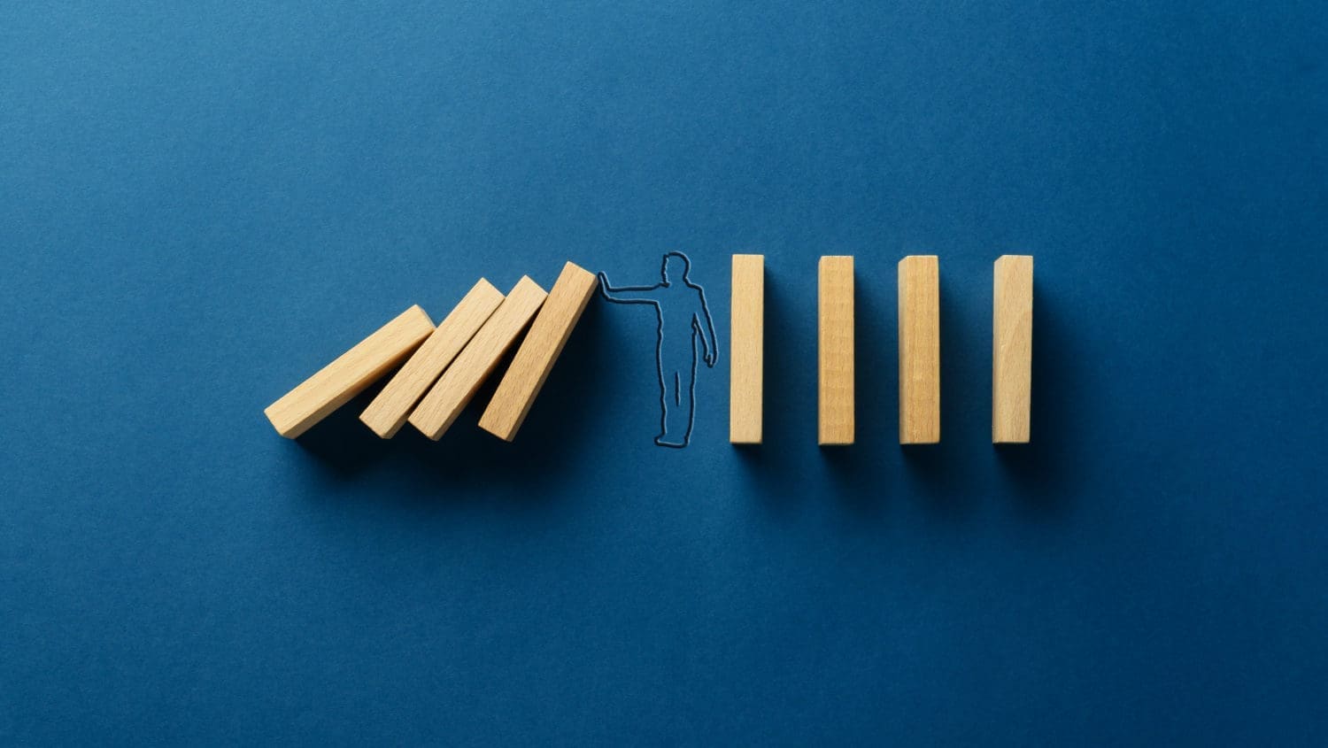 A man is standing in front of wooden dominoes on a blue background.