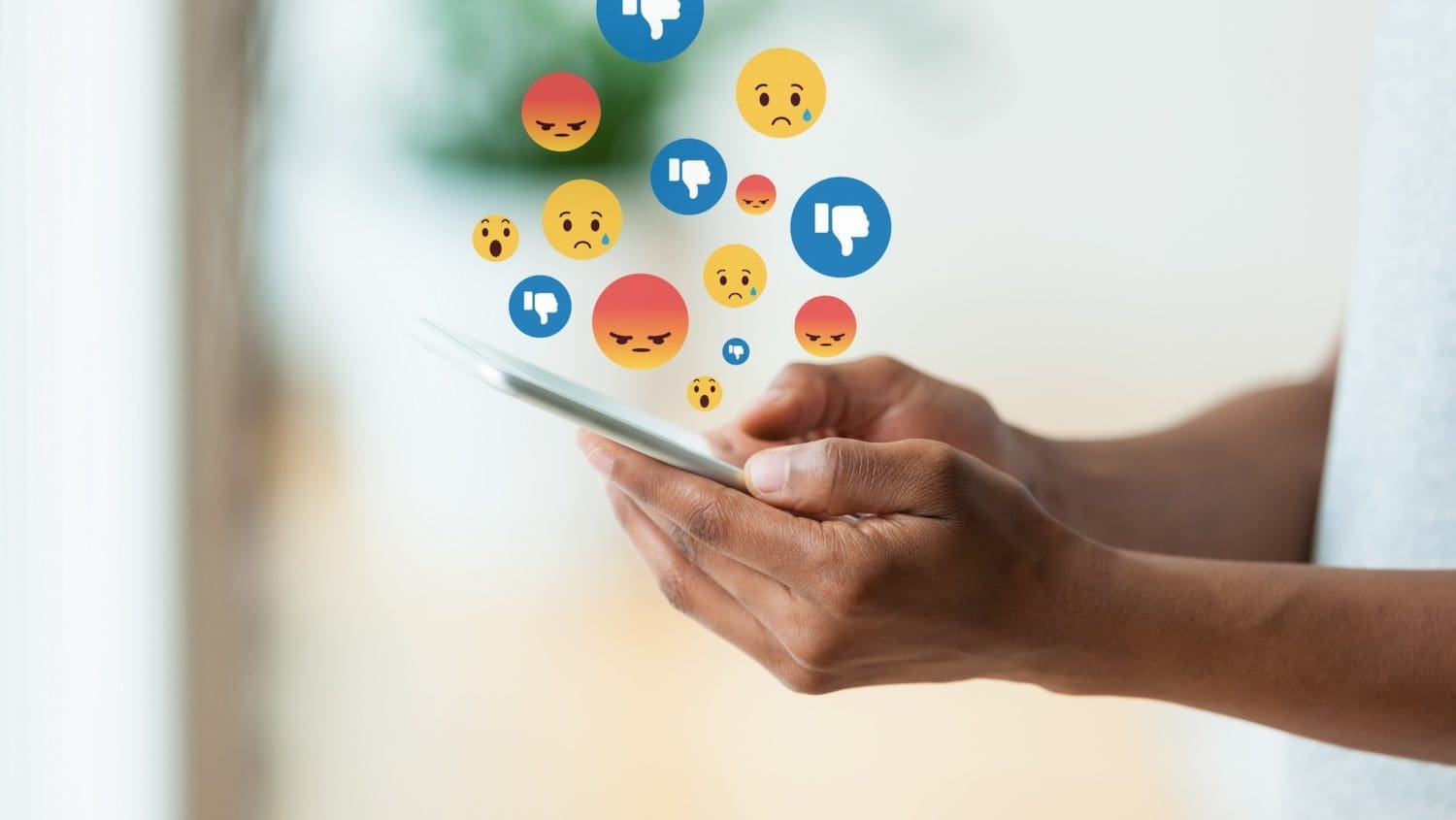 A person holding a smartphone with emoticons coming out of it, illustrating the negative impacts of social media on business.