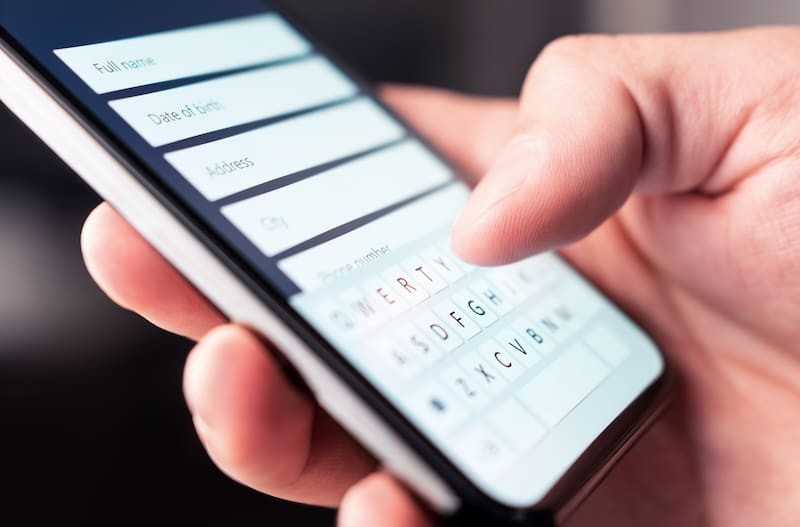 A person is holding a smartphone and typing on the keyboard to remove personal information from Google.