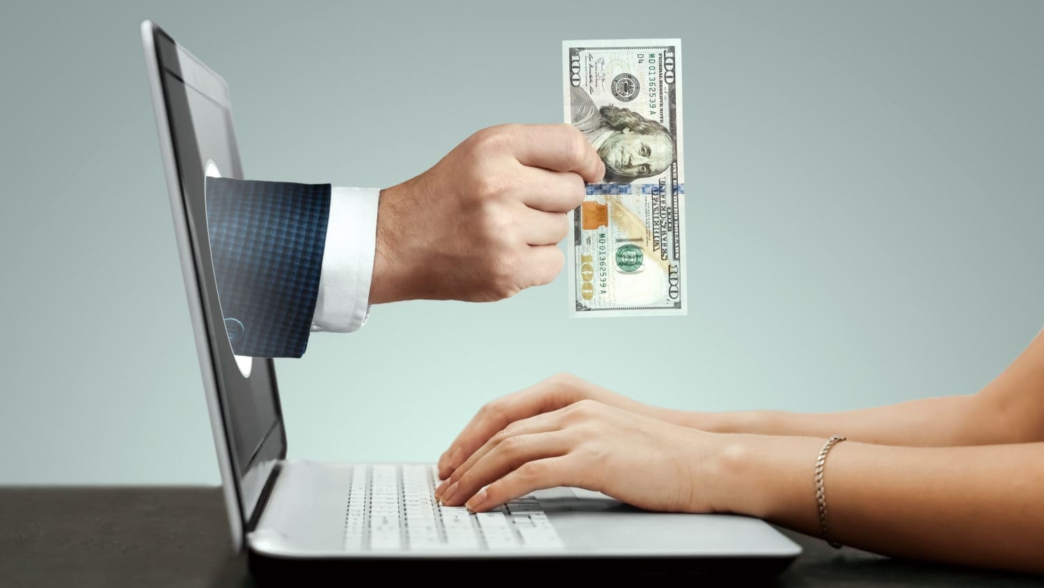 A woman is holding a dollar bill in front of a laptop.