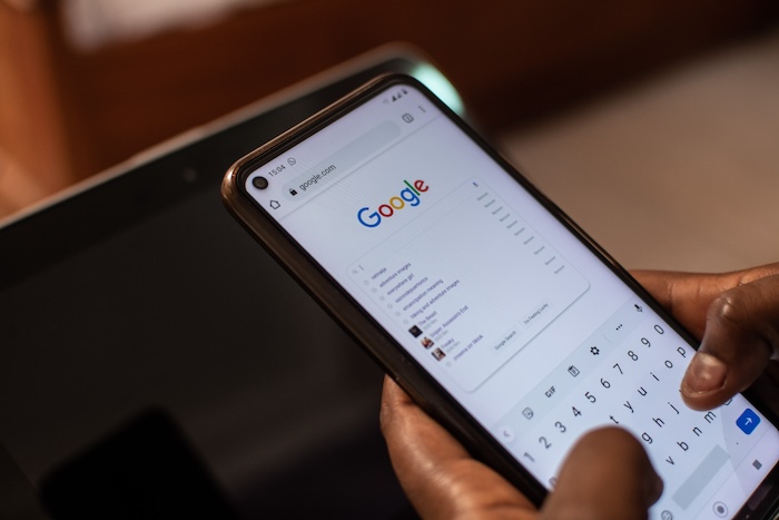 A person holding a phone displaying the Google logo, determined to remove Ripoff Reports.