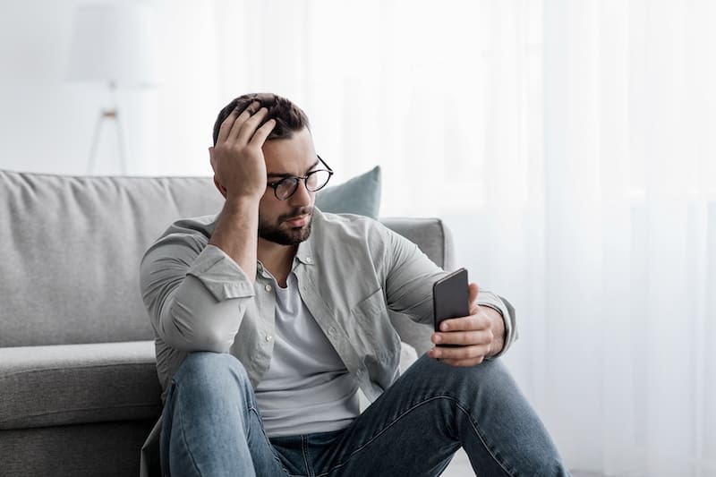 A man sitting on the couch looking at his phone while searching for instructions on how to remove articles from the internet.