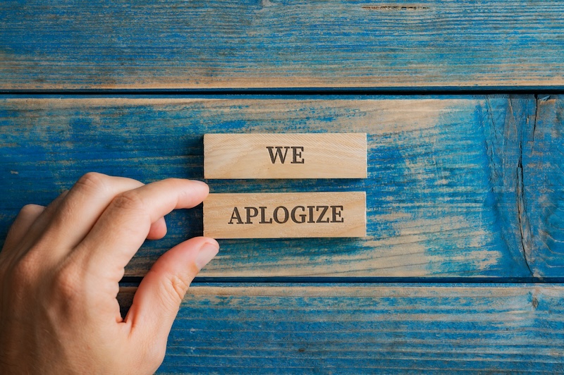 A hand holding a wooden block imprinted with the word "apologize" as part of an effort to restore its online reputation.