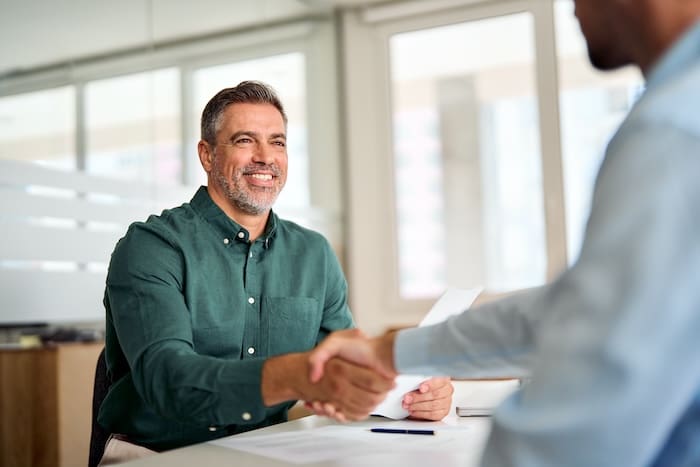 A man shaking hands with another man in an office, discussing business and potentially seeking advice from reputation management consultants.