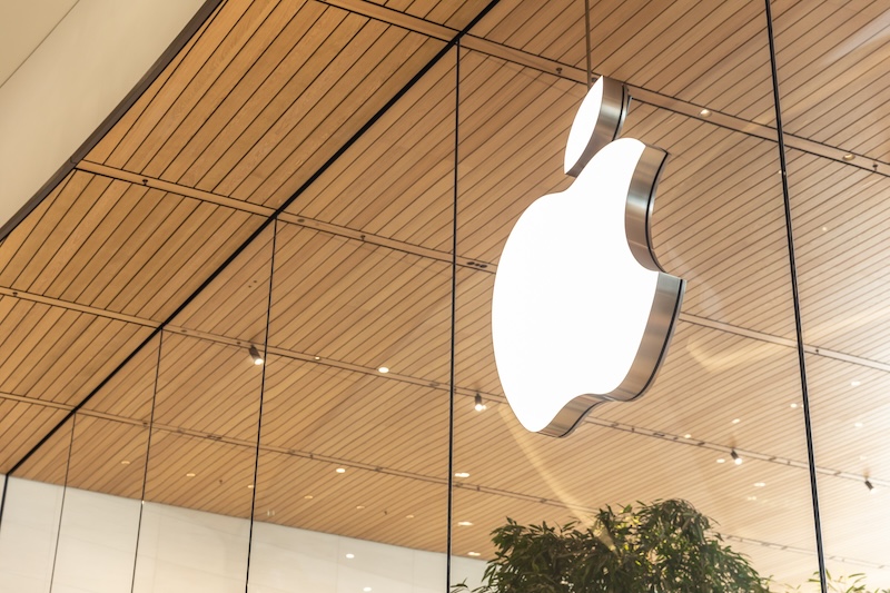 Illuminated apple logo, symbolizing one of Fortune's Most Admired Companies, on the exterior of a modern store, set against wooden panels and glass backdrop.
