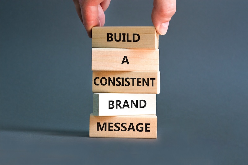 A hand stacking wooden blocks with the words "build a consistent online reputation" written on them, against a plain gray background.