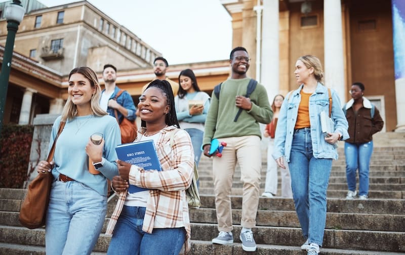 A group of students walking down stairs in front of a college building.