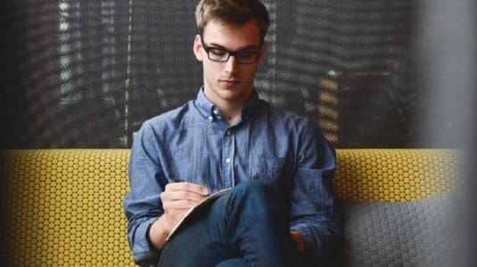 young professional man writing in notebook on a couch