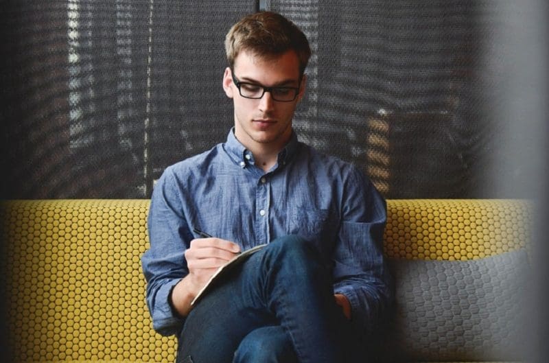 young professional man writing in notebook on a couch