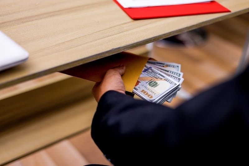 A person embezzles money at work by putting a stack of cash in a hiding spot under their desk.