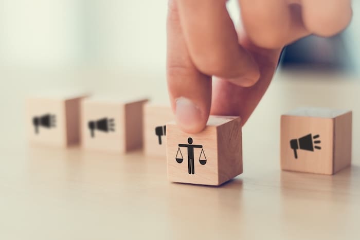 A hand is pushing a wooden block with a legal symbol on it.