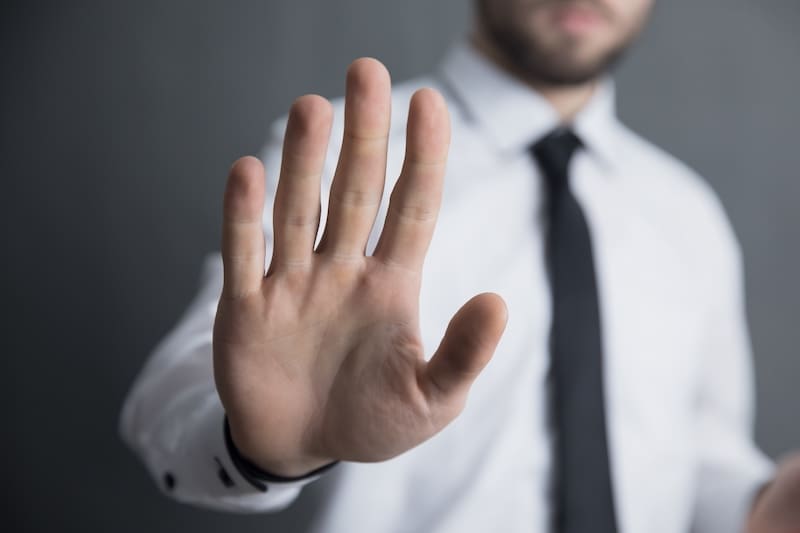 A businessman in a dress shirt and tie holds his right hands up to signal "stop."