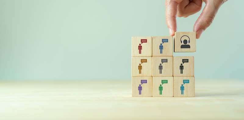 A hand placing a wooden block with a reputation management tips icon onto a pyramid of blocks, each featuring a colorful silhouette of a person, symbolizing team building or human resources.
