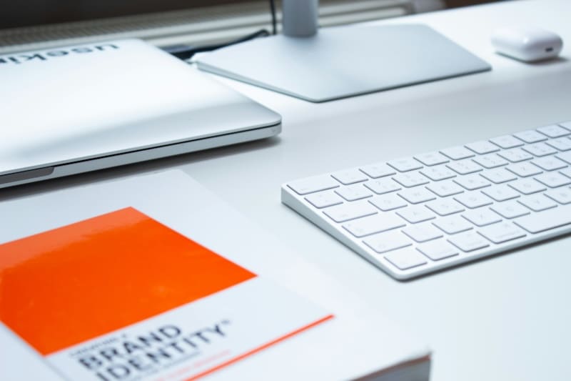 A modern workspace with a "brand reputation management" book, a white laptop, keyboard, and mouse on a sleek desk. A calm and organized office setting.