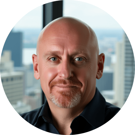 A bald man with a goatee and mustache, wearing a dark shirt, smiles slightly in front of a window with a cityscape in the background, reflecting his team spirit and collaborative nature.