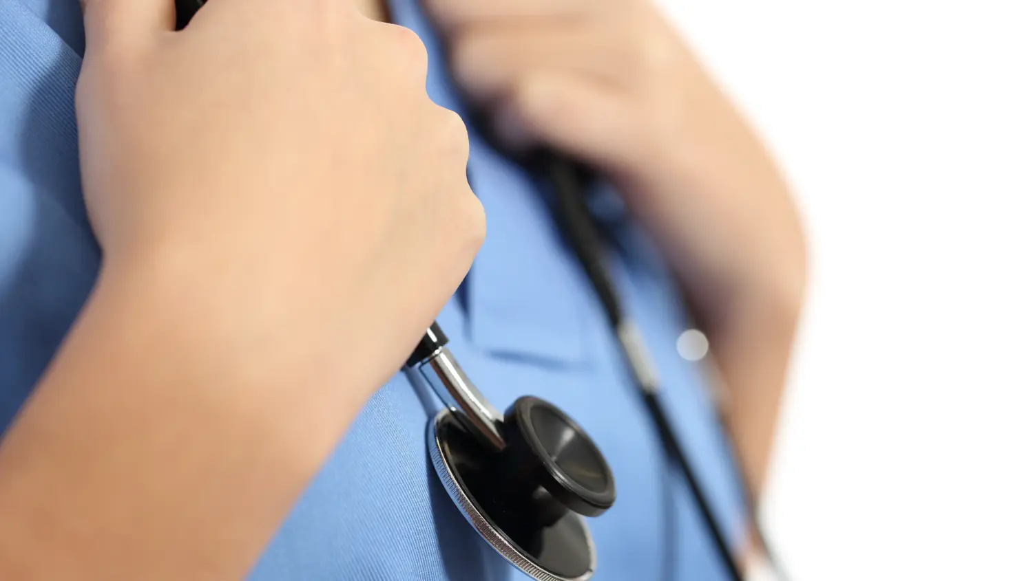 A person in blue scrubs holds a stethoscope against their chest, suggesting a healthcare professional. The background is white and out of focus.