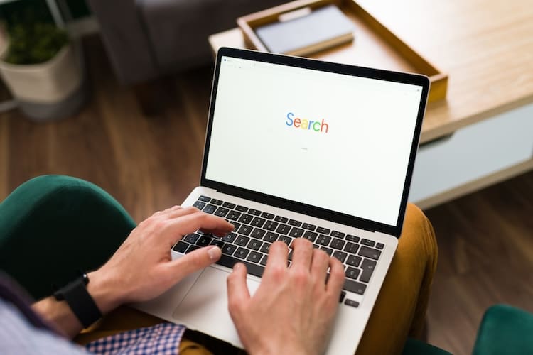 A person sitting with a laptop on their lap, about to type an unwanted search query into Google.