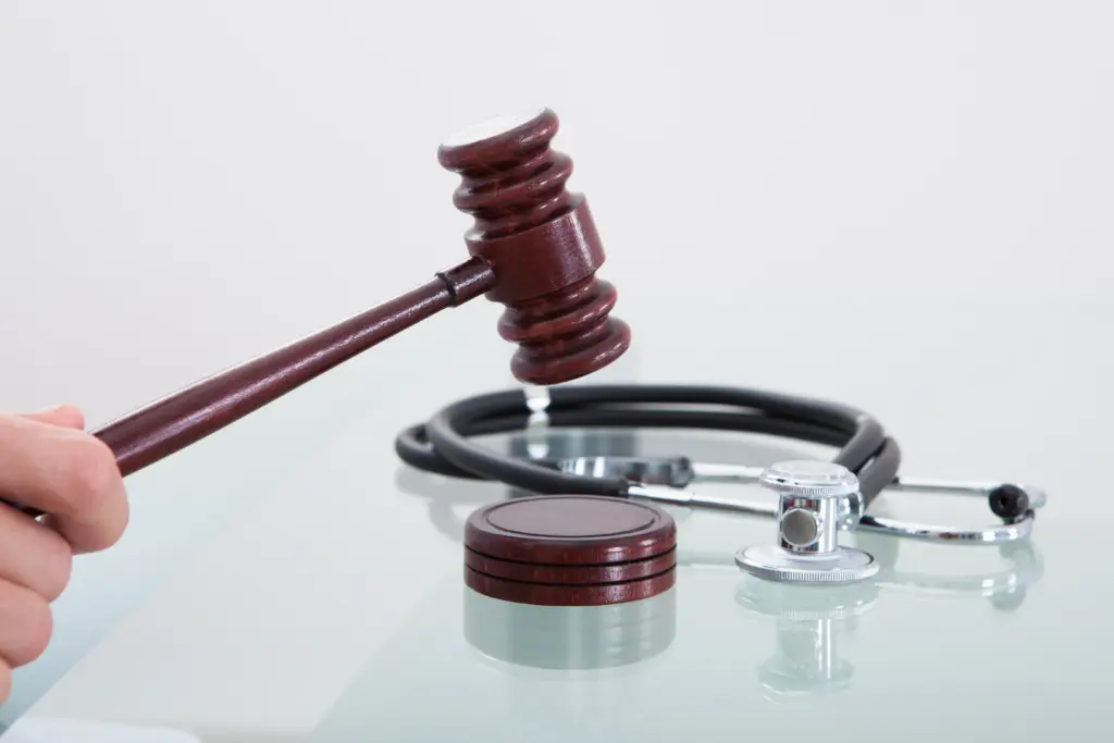 A wooden gavel is being struck near a stethoscope on a glass surface, symbolizing the intersection of law and medicine.