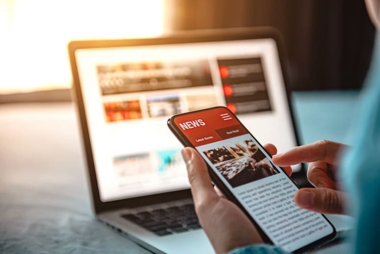 Keeping updated on the go: a person browsing the latest news on a smartphone with a laptop displaying unwanted Google search results in the background.