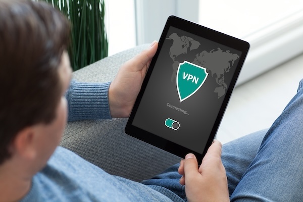 A man sitting on a couch using a tablet with a vpn icon for online privacy.