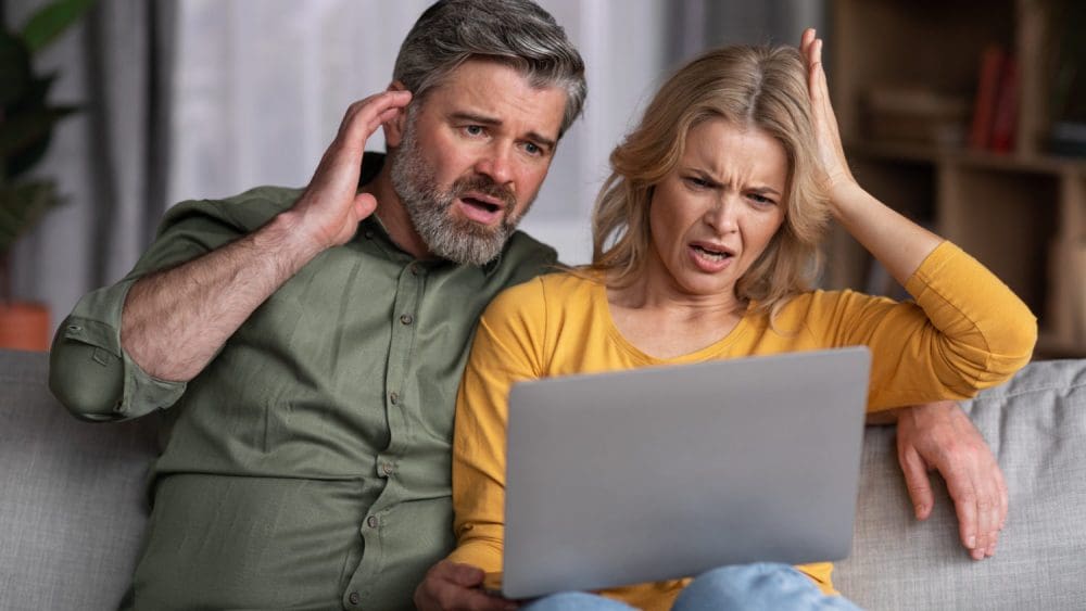 a man and woman sitting on a couch looking at a laptop.