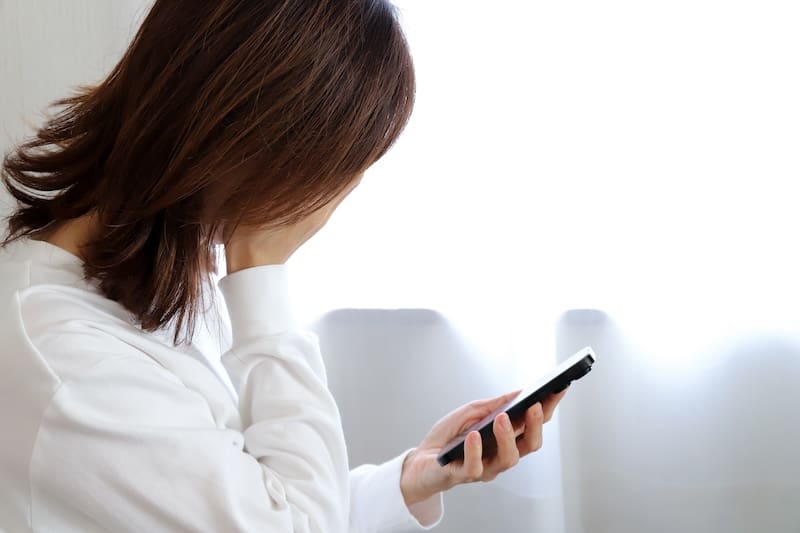 A woman looking at her phone while sitting in front of a window.