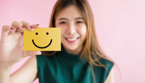 woman holding up smiley face card yellow
