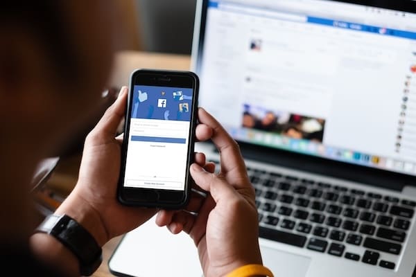 A person holding a cell phone browsing Facebook while removing personal information from the internet.