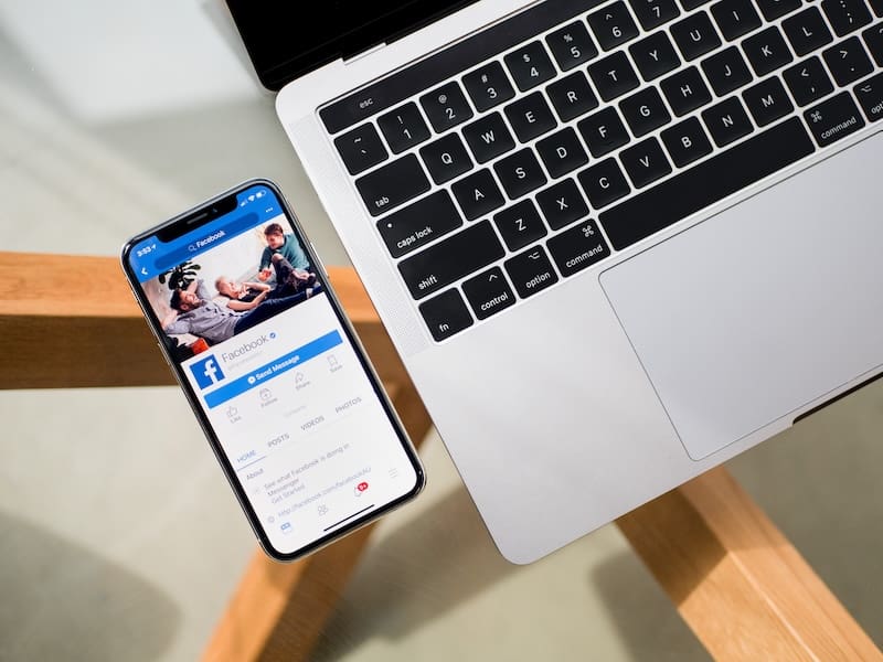 A phone showing Facebook next to a laptop.