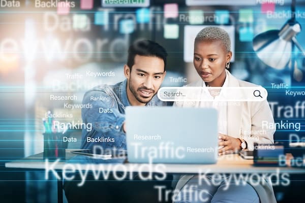 Two professionals analyzing data on a laptop with digital marketing terms related to what makes a brand strong superimposed in the background.